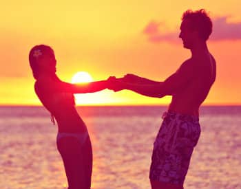 Silhouette of man and woman facing each other holding hands amidst the setting sun over the ocean