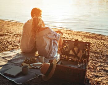 Man and woman having a picnic on the beach with the sun's rays shining on the water