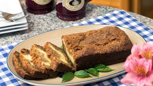 Loaf of banana bread with cream cheese filling on an oval plate that is on a blue checkered cloth