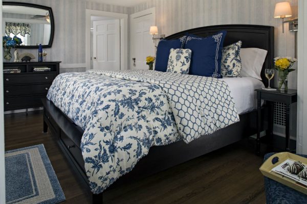 Elegant guest room with dark brown sleigh bed, blue and white bedding, wood floors, and dresser with mirror