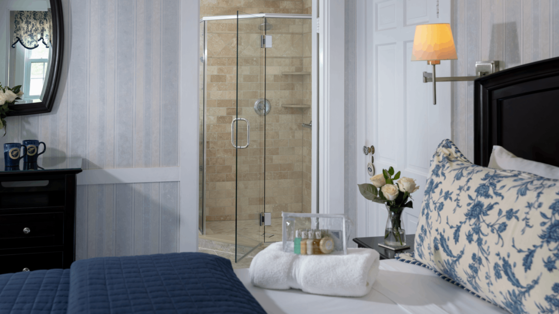 Bedroom with bed with white and navy linens, towels on the bed fresh flowers and view of the bathroom