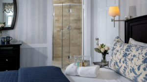 Bedroom with bed with white and navy linens, towels on the bed fresh flowers and view of the bathroom 