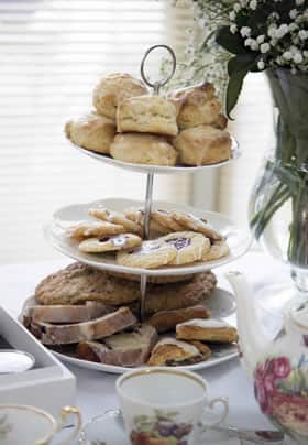 Three tiered dessert tray topped with sweet rolls, cookies, and sweet breads near tea service