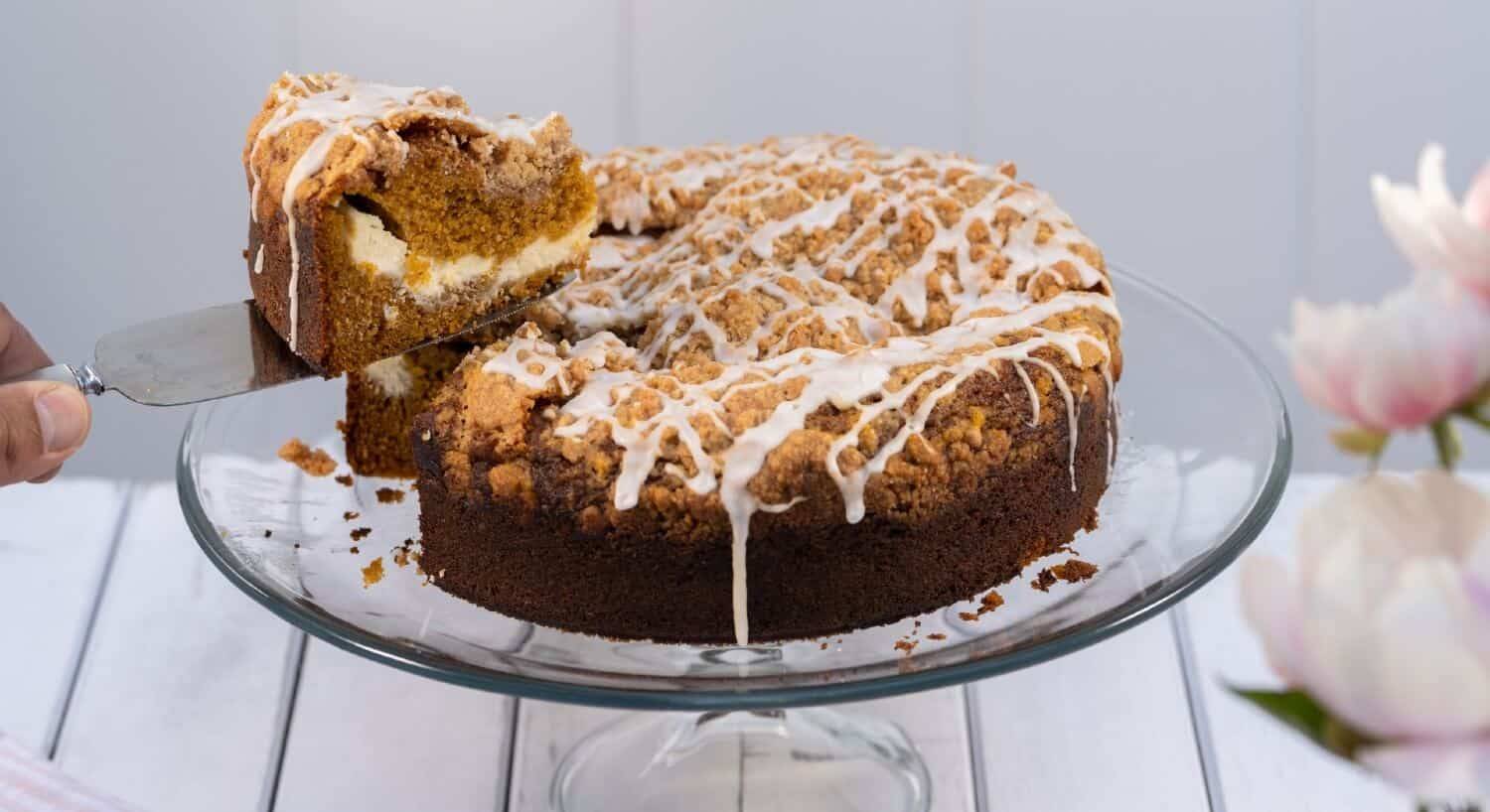 Round coffee cake drizzled with frosting sitting on a glass cake platter