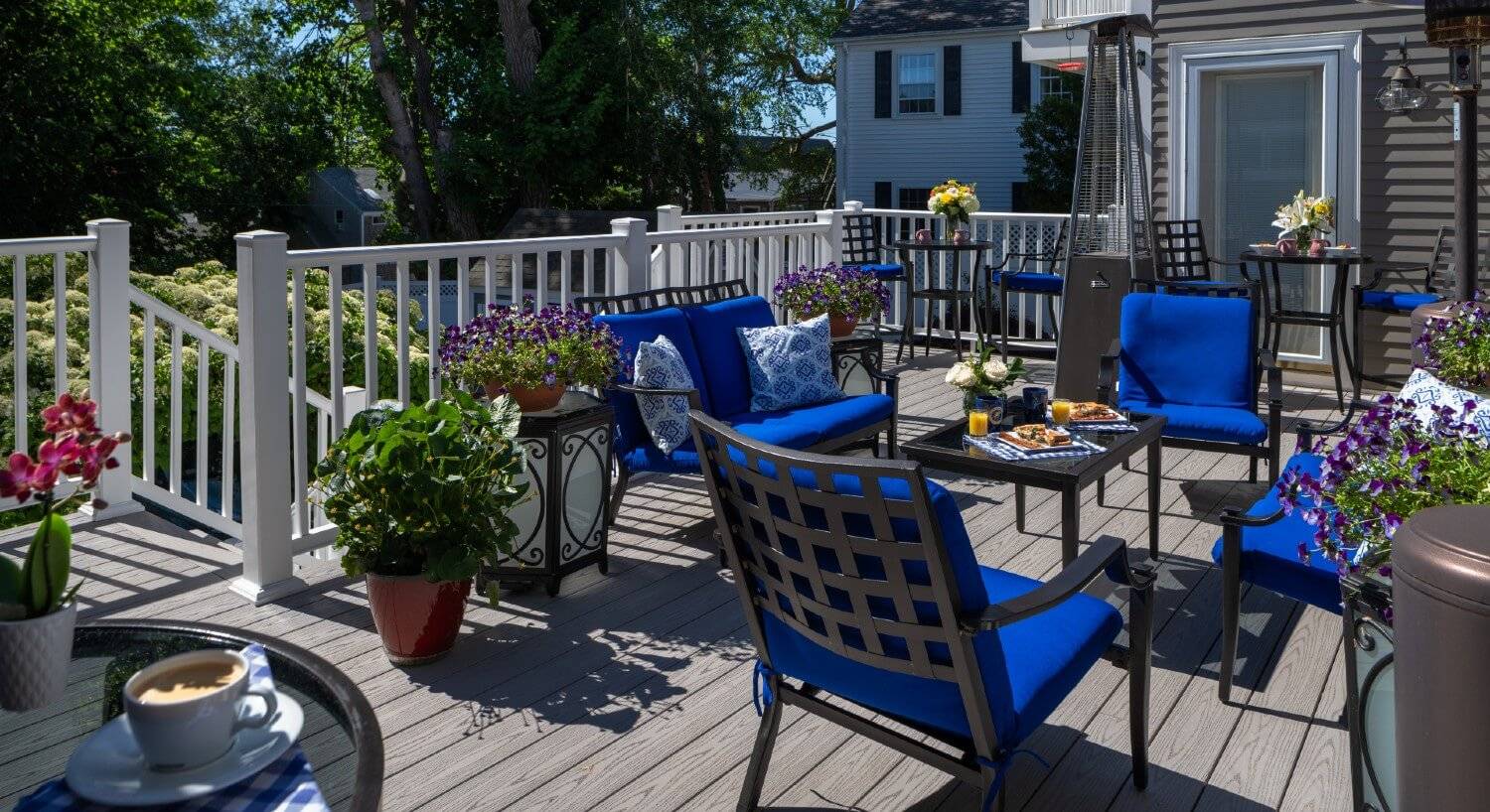 A large outdoor deck with patio furniture with blue cushions and lots of fresh pots of flowers