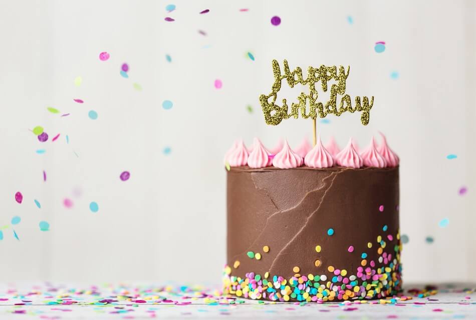 Cake with chocolate and pink frosting with gold happy birthday sign and confetti in the air