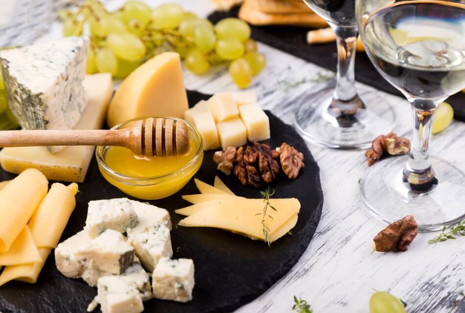 Black platter of various cheeses, nuts and small bowl of honey