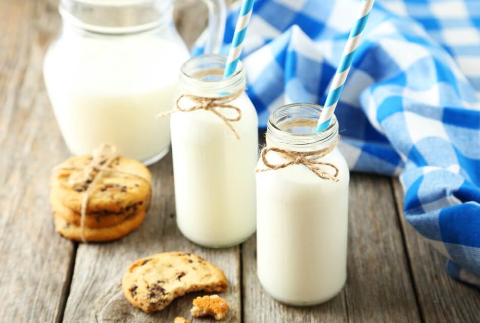 Two glass jars of milk with striped straws next to a stack of cookies