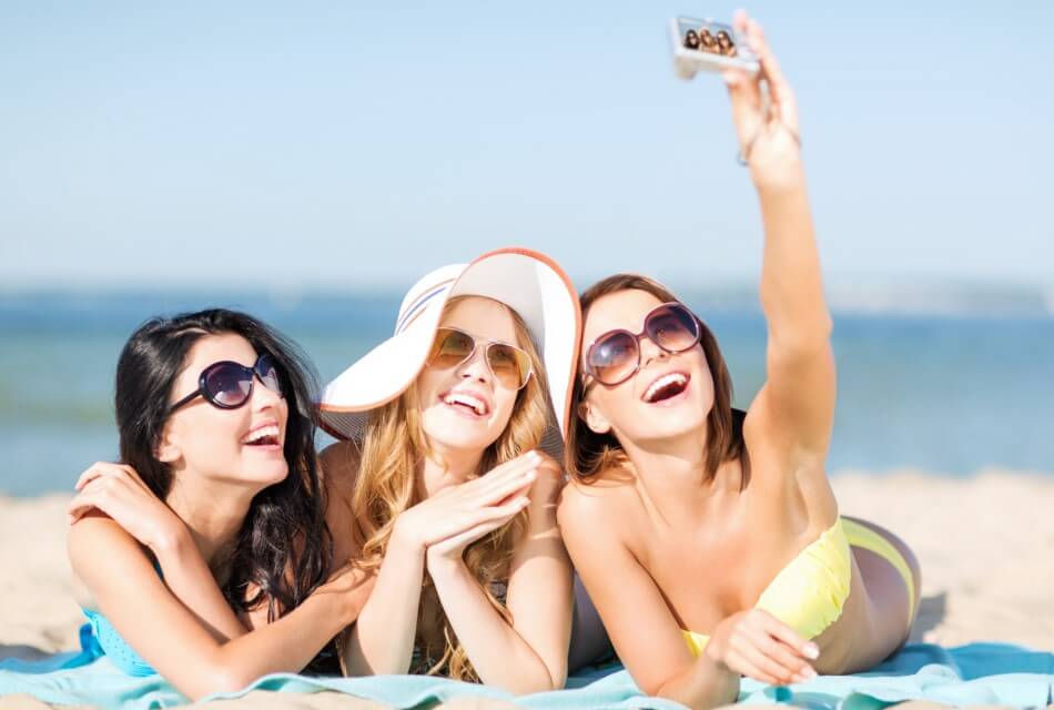 Three girlfriends laying on a beach taking a selfie