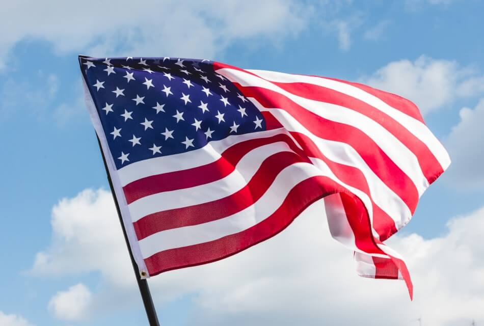 Red, white and blue American flag against a blue sky with clouds